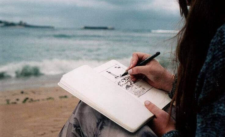 nainen piirtää rannalla