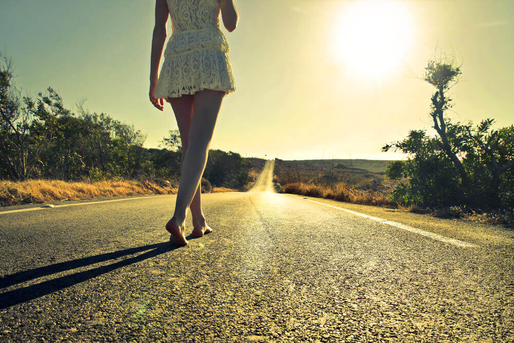 nainen kävelee maantiellä paljain jaloin