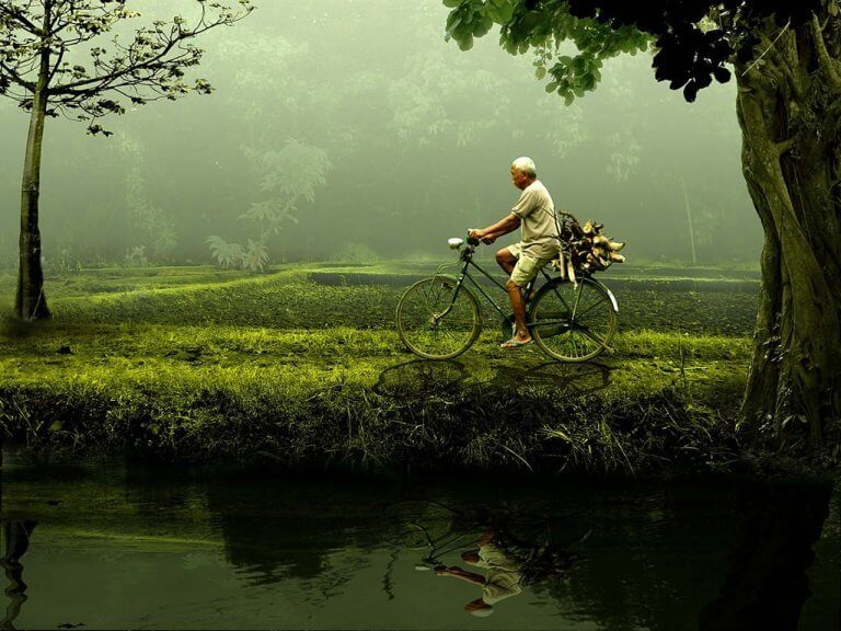 vanha mies pyöräilee joen varrella