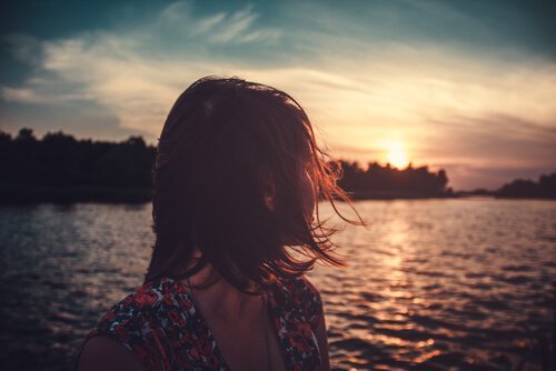 nainen katsoo järvelle ilta-aurinkoon