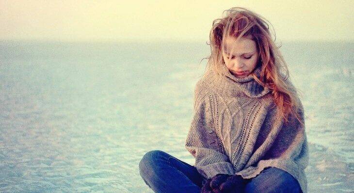 masentunut äiti istuu yksin rannalla