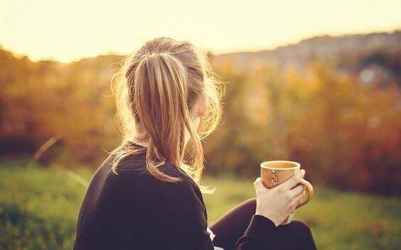 nainen istuu ulkona ja juo kahvia