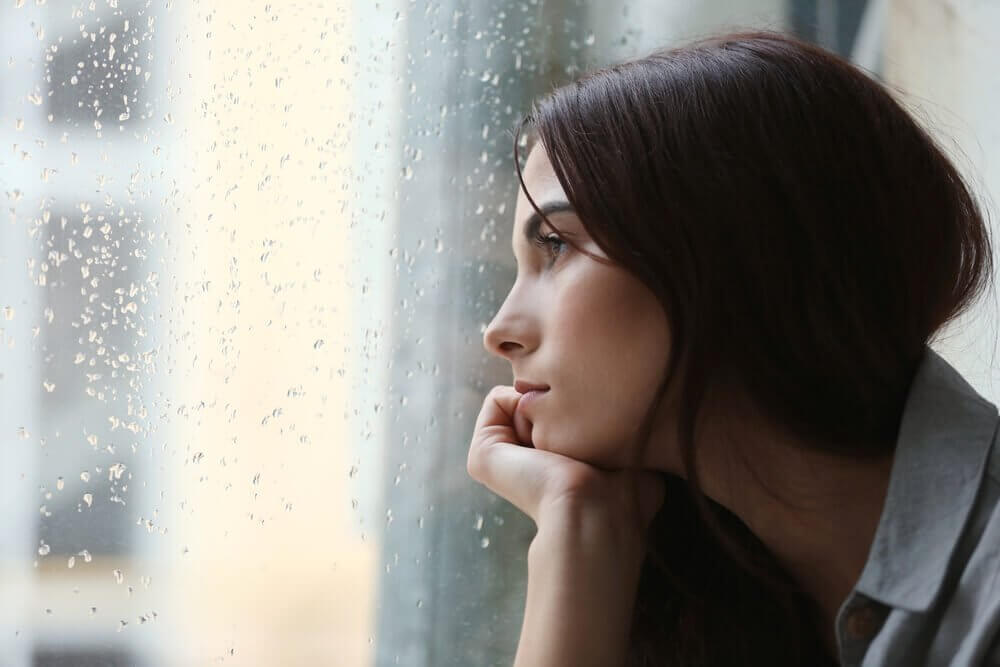 nainen katsoo ikkunan läpi sateeseen
