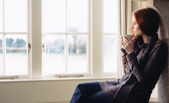 nainen juo teetä ikkunan edessä