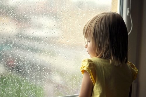 pieni tyttö katselee sateisen ikkunan läpi