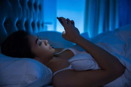 Nainen räplää puhelinta yöllä sängyssä.